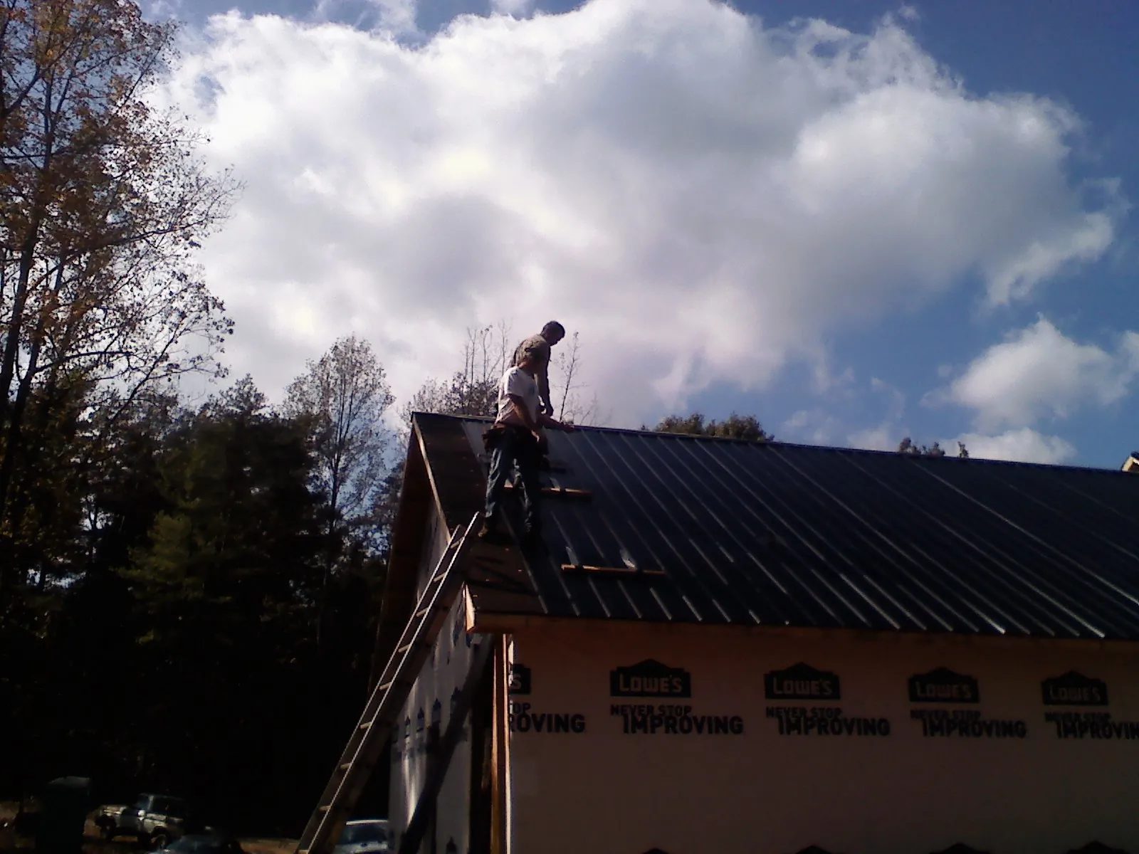 Roofer fastening dark metal panels high against a cloudy sky, from a Roof Inspection job in Cumberland Furnace