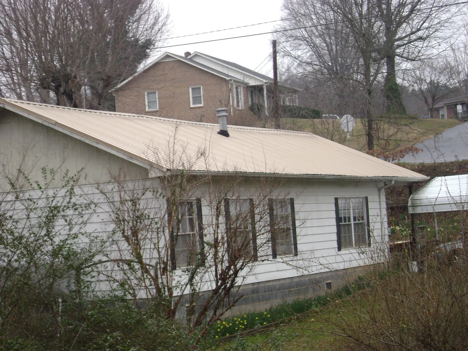 Tan metal roof on a white sided house set into a hillside — Commercial Roofing by Roofing Brothers in Cumberland Furnace